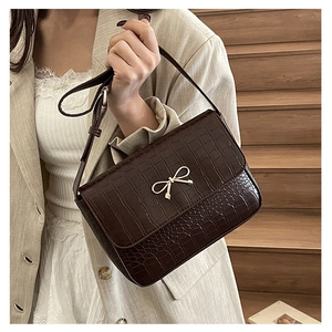 Détail d'un sac à main marron foncé à motif crocodile avec fermoir nœud doré chic