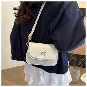 Detail of white leather crossbody bag with golden butterfly buckle worn by a model