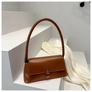 Detail of a brown leather baguette bag featuring bronze hardware on a minimalist background