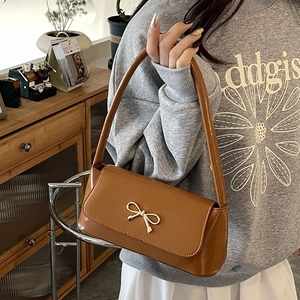 Sac baguette en cuir marron avec nœud doré présenté dans un cadre chaleureux