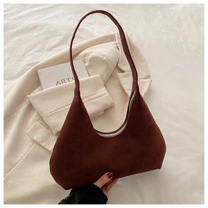 Détail d'un sac hobo en daim marron avec fermeture éclair argentée sur un blazer beige
