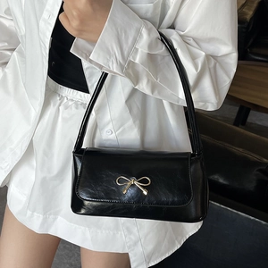 Sac baguette noir brillant avec fermoir nœud doré porté à l'épaule pour un style chic
