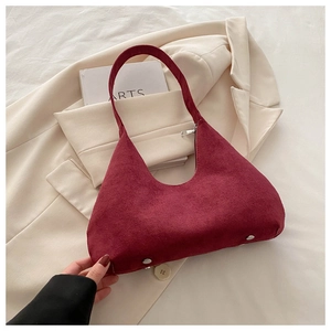 Détail d'un sac bandoulière en daim bordeaux montrant des clous en argent sur un blazer