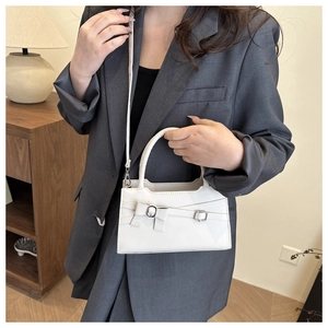 Detail of white glossy mini crossbody bag with a decorative bow on grey blazer outfit