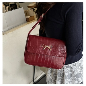 Détail d'un sac bandoulière bordeaux motif crocodile avec boucle noeud dorée sur modèle