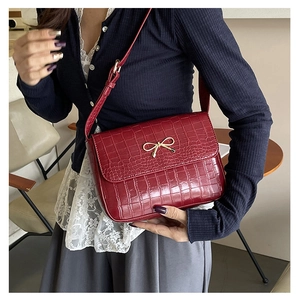 Détail du sac bandoulière bordeaux motif crocodile avec un fermoir nœud doré élégant