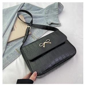 Détail du sac bandoulière noir motif crocodile avec boucle dorée en forme de nœud