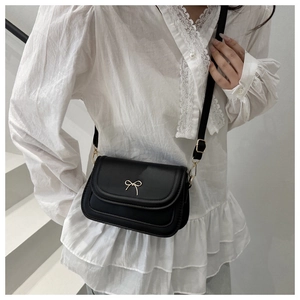 Close-up of black matte leather shoulder bag featuring a gold metal bow and detailed stitching