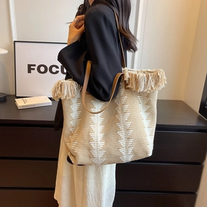 Large woven canvas tote bag with bohemian tassels and brown leather straps for commuting