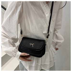 Close-up of black matte leather mini square bag with golden bow buckle on lace shirt