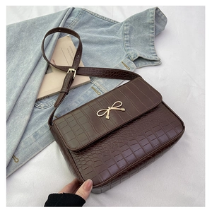 Détails d'un sac marron foncé avec motif crocodile et boucle dorée en nœud
