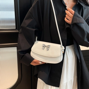 Detail showing the white crossbody bag with a delicate silver metal bow on the flap