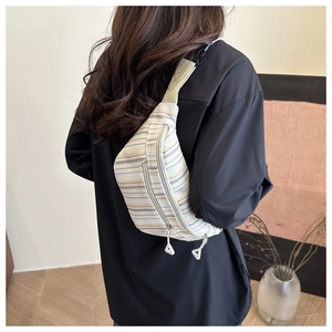Détail d'un sac bandoulière rayé porté sur une chemise noire de coupe oversize