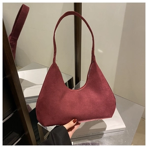 Sac hobo en daim bordeaux avec clous de fond argentés posé sur table en verre