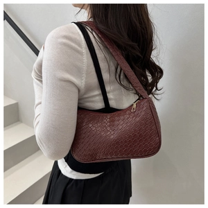 Close-up of woven texture on dark brown baguette shoulder bag with gold zipper detail