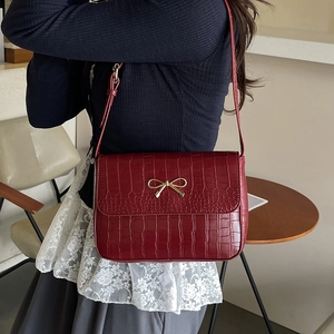 Sac bandoulière bordeaux élégant avec motif crocodile et boucle dorée porté par un mannequin