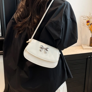 Detailed view of white faux leather crossbody bag with silver bow on a person