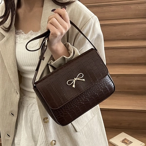Sac carré marron à motif crocodile avec nœud doré porté par un mannequin élégant