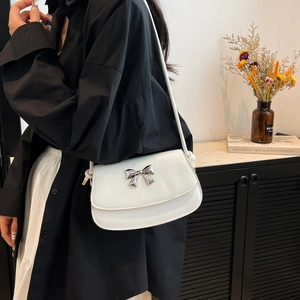 Close-up of a white shoulder bag featuring a metallic silver bow and sleek minimalist design