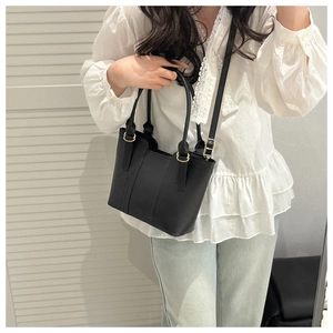 Détail d'un sac seau en cuir noir avec ferrures dorées porté par un mannequin en tenue
