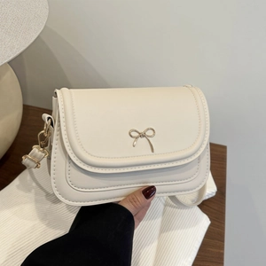 Minimalist off-white leather underarm bag with gold bow clasp and adjustable strap