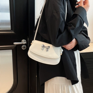 Detailed view of a white crescent shoulder bag featuring a metallic silver bow accent