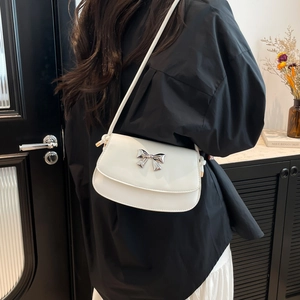 Detailed view of a white glossy patent leather bag with a silver metal bow buckle