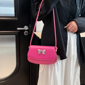 Side view of model wearing a rose pink leather shoulder bag with silver metallic bow buckle
