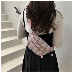 Gros plan d'un sac de poitrine en toile rayée rose et gris avec bandoulière en nylon