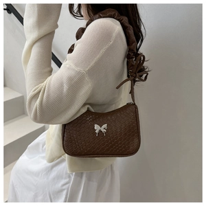 Détail du sac à bandoulière tissé marron avec boucle papillon et bandoulière à volants