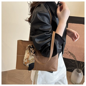 Detail of vintage brown leather tote bag featuring a decorative silk scarf on the handle