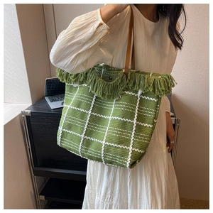 Detail of a woven tote bag with green and white plaid pattern and stylish fringe trim