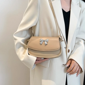 Detail of minimalist beige leather shoulder bag with a silver metal bow buckle accent