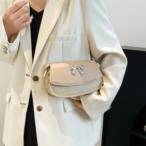 Model wearing a minimalist beige shoulder bag with a silver metal bow accent