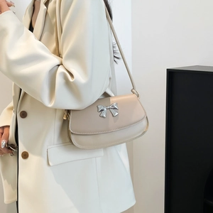 Detailed view of beige faux leather shoulder bag featuring a silver metal bow buckle