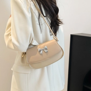 Model wearing a beige shoulder bag with silver bow accent and smooth leather finish