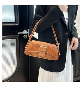 Detail of a brown croc-embossed shoulder bag with a gold buckle on white dress