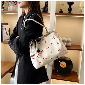 Detail of white corduroy tote bag with cherry prints and woven handle featuring a silk scarf