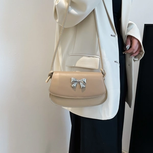 Close-up of beige shoulder bag with silver bow buckle worn with a white blazer