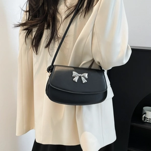 Detail view of black shoulder bag with silver bow accent on a white blazer outfit
