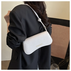 Detail of white crocodile embossed baguette bag worn over the shoulder by a model