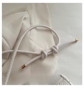 Detail of woven white leather shoulder strap with golden metal caps and knotted design