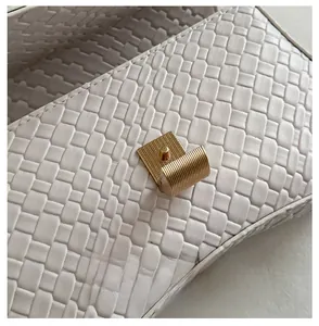 Close-up of golden cylindrical metal clasp on white woven leather shoulder bag