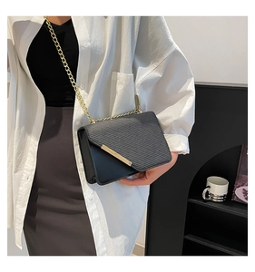 Detail of black crossbody bag featuring textured leather panels and gold chain strap