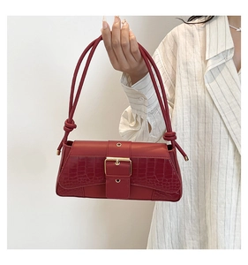 Detail of red crocodile texture baguette bag with golden metal buckle and knot strap