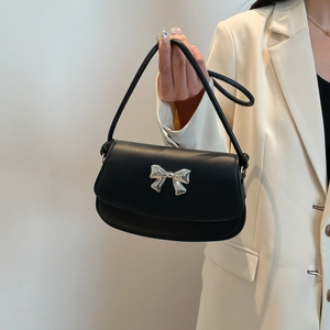 Detail view of a black leather shoulder bag with a silver metallic bow on model in beige blazer