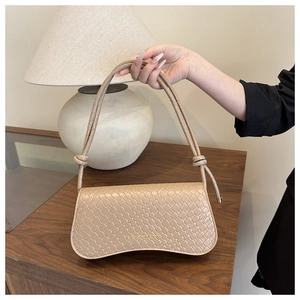 Detail of beige woven square bag featuring a gold fashion logo and a knotted handle strap