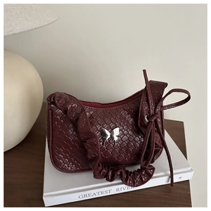 Détail d'un sac à bandoulière bordeaux tressé avec papillon argenté et bandoulière plissée