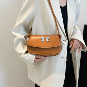 Detail view of orange leather saddle bag with silver bow ornament worn with white blazer