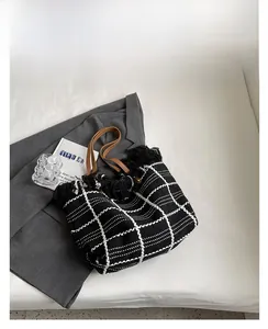 Close-up of black and white checkered woven tote bag with fringe and brown leather handles